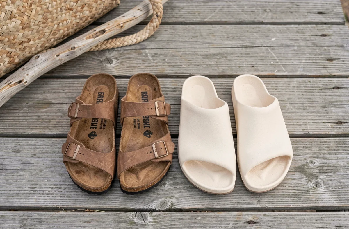 Comparaison côte à côte de sandales Birkenstock Gizeh et Billowy posées sur une promenade en bois usé avec un sac de plage